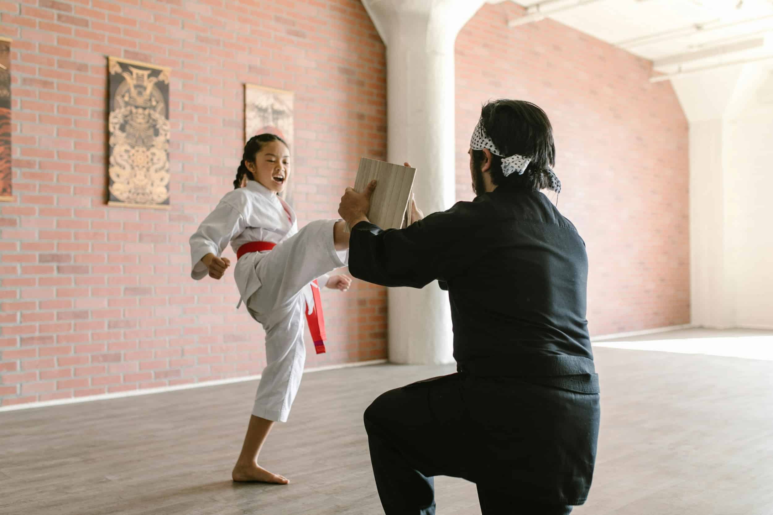 Young Moores Martial Arts Academy student kicking board with instructor